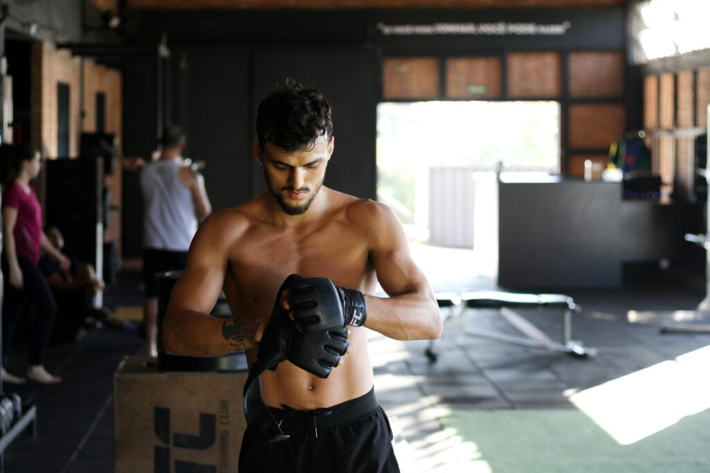 Shirtless man preparing for an intense workout session in a gym, wearing boxing gloves.